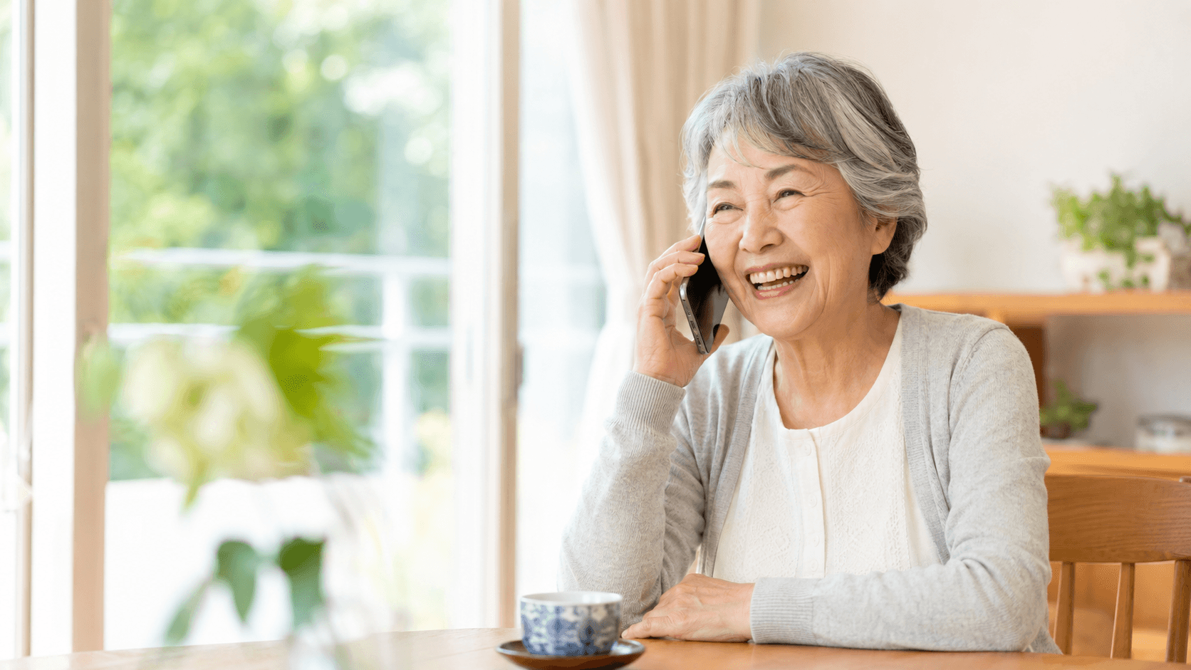 70代の女性がリビングで電話しながら笑顔で話している